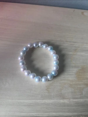 Elastiskt pärlarmband i vitt - Säljer ett stilrent armband med vita, runda pärlor trädda på elastisk tråd. Perfekt accessoar för dig som gillar klassisk och enkel stil. Pärlorna har en fin glans och armbandet är lätt att ta på och av.