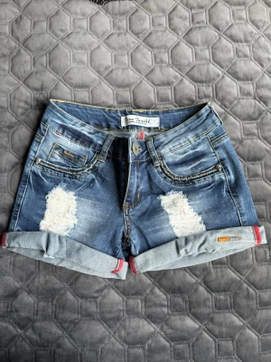 Jeansshorts  - Blå jeansshorts med trasiga detaljer, storlek w26 som motsvarar xs