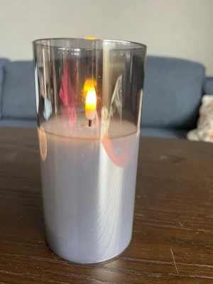 Grå LED-ljuslykta i glas - Snygg LED-ljuslykta i cylinderformad gråtonat glas. Ger ett mysigt sken med sin realistiska låga och passar perfekt som dekoration i fönster eller på bord. Drivs av batteri och är enkel att flytta runt efter behov. Klistermärken vid batteri-luckan och vid ena sidan glaset, men kan lätt tas bort med en lätt fuktad trasa. 