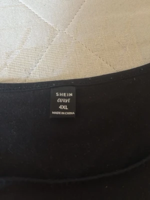 Svart linnetopp med röd drake Shein - Cool svart linnetopp från Shein Curve med ett rött drakmotiv och texten 'Confidence' framtill. Toppen är ärmlös och har en avslappnad passform, perfekt för att ge din outfit edge. Materialet känns mjukt och lätt mot huden.