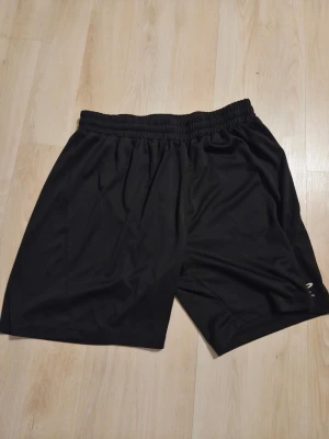 Svarta träningsshorts från Energetics - Säljer ett par svarta träningsshorts från Energetics. De har elastisk midja och är gjorda i ett lätt och snabbtorkande material, perfekt för gym eller löpning. Klassisk design med diskret logga på benet.