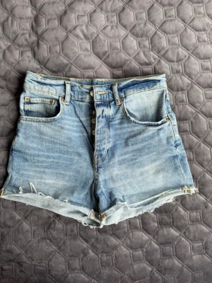Blå jeansshorts  - Blå jeansshorts, femficksmodell och knäppning med flera knappar framtill.