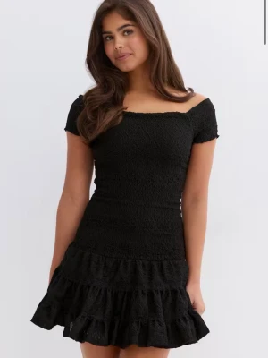Svart offshoulder kortklänning - Säljer en svart kortklänning med offshoulder och volangkant nertill. Klänningen har en smockad, figurnära passform och är tillverkad i ett broderat material som ger en romantisk känsla. Perfekt för dig som vill ha en trendig och bekväm look. Helt ny med lappar kvar!!