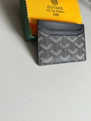 Svart Plånbok - Snyggt svart och unik plånbok med det klassiska vita mönstret och loggan framtill. Fodralet har flera kortfack och är gjort tåligt material Perfekt för dig som vill ha en stilren och exklusiv accessoar.
