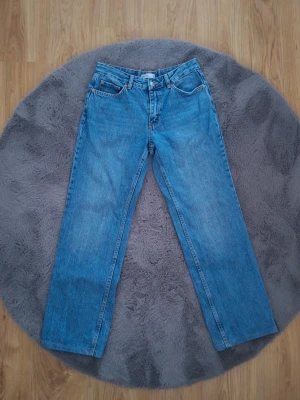 Blå raka jeans med låg midja - Klassiska blå jeans med rak passform och låg midja. Jeansen har fem fickor och stängs med dragkedja och knapp. Tillverkade i slitstark denim som ger en tidlös look. Perfekta för dig som gillar en enkel och clean stil.