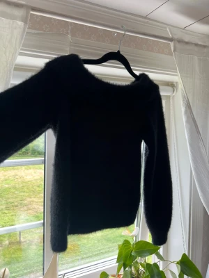 Svart fluffig stickad tröja - Mysig svart stickad tröja med fluffig yta och rund halsringning. Tröjan har långa ärmar och en enkel, rak passform. Perfekt för dig som gillar en stilren och bekväm look. 