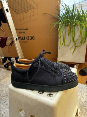 Svarta sneakers med nitar - Säljer ett par svarta sneakers med coola nitar på tån och ovansidan. Skorna har en låg profil, rund tå och snörning framtill. Materialet ser ut att vara mocka vilket ger en lyxig känsla. Perfekta för dig som vill sticka ut med din stil.