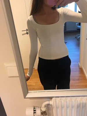 Vit långärmad topp med rund ringning - Snygg vit långärmad topp med rund, djup ringning. Modellen är tight och smickrande, perfekt att styla med jeans eller kjol. Tillverkad i mjukt bomullsmaterial som känns skönt mot huden. Finns en liten fläck som knappt märks (bild 5)