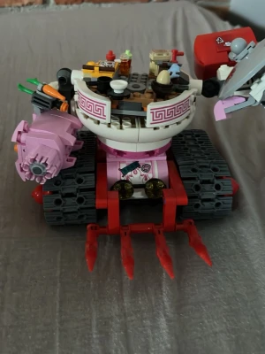Färgglad LEGO-robot  - Unik LEGO-robot i vitt, rosa och rött med larvfötter och detaljer som köksredskap, mat och verktyg. Roboten har armar med sköld och klo, samt dekorationer som morötter och tallrikar. Perfekt för dig som gillar kreativa byggen och coola detaljer.