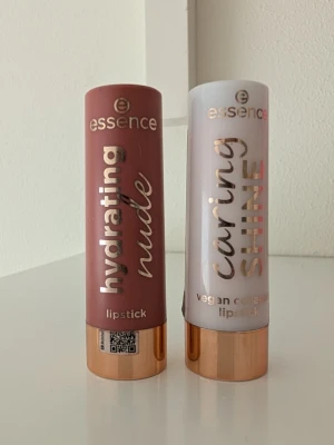 Essence hydrating & caring läppstift - Två läppstift från Essence: ett hydrating nude i en mjuk brunrosa ton och ett caring shine i en ljusare, skimrande nyans. Båda har elegant hylsa med roséguld-detaljer och är i klassisk stickform. Caring shine är vegansk och collagen-berikad. Lite använda. Caring Shine 202 och Hydrating Nude 303