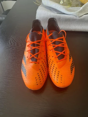 Addias elites  - Säljer ett par riktigt snygga fotbollsskor i stark orange färg med svarta detaljer och mönster. Skorna har snörning och en modern, strömlinjeformad design med dobbar för bra grepp på planen. Perfekta för dig som vill sticka ut på fotbollsplanen!