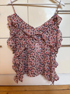 Blommig volangtop med tunna axelband storlek XS från Zara. Ny, oanvänd! - Söt blommig topp med volangdetaljer och tunna axelband. Toppen har ett luftigt fall och små blommor över hela tyget. Storlek XS, från Zara. Ny, oanvänd och är i perfekt skick!