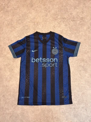 Inter Milan matchtröja blå/svart - Snygg Inter Milan matchtröja från Nike i blått och svart med vertikala ränder. Tröjan har trycket 'betsson sport' på bröstet, klubbmärke och två stjärnor. På ryggen står det 'Lautaro' och nummer 10. Tillverkad i lätt och ventilerande Dri-FIT-material.