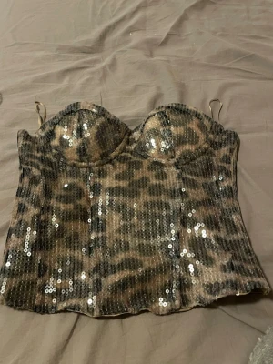 Leopardmönstrad paljettbustier - Säljer en snygg bustier topp med leopardmönster och glittriga paljetter. Toppen har tunna axelband, vadderade kupor och en figurnära passform. Perfekt för dig som vill sticka ut och älskar djurmönster och glitter.