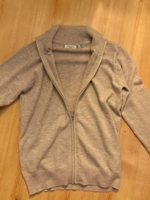 Beige ziptröja från RYVLS - Beige ziptröja från RYVLS Stockholm med hög krage och ribbade muddar. Tröjan är i mjukt material och har en stilren look som passar perfekt till lager-på-lager. Enkel att matcha med jeans eller chinos.