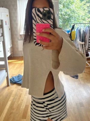 Beige stickad tröja med slits - Trendig beige stickad tröja med hög hals och breda ärmar. Tröjan har en cool slits på sidan som ger en avslappnad och modern look. Perfekt att styla med jeans eller kjol för en chill vibe.