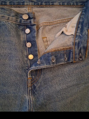 Blå raka jeans med knäppning - Klassiska blå jeans i rak modell med knappgylf och fem fickor. Jeansen har en tidlös tvätt och är gjorda i kraftigt denimtyg. Perfekta för dig som gillar en enkel och clean look.