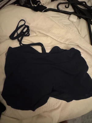 Mörkblå linnetopp med smala band - Säljer en mörkblå linnetopp med smala axelband och lätt rynkad detalj framtill. Toppen har en enkel och stilren design, perfekt för varma dagar. Materialet känns mjukt och lätt mot huden.
