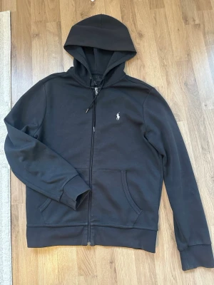 Svart hoodie från Polo Ralph Lauren - Säljer en svart hoodie från Polo Ralph Lauren med dragkedja framtill och klassisk huva. Skriv gärna vid frågor