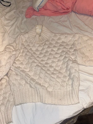 Vit stickad tröja från Monki - Säljer en chunky vit stickad tröja från Monki i storlek S. Tröjan har ett snyggt bubbligt mönster, ribbad halsringning, muddar och nederkant. Perfekt för att hålla sig varm och stilsäker under kyliga dagar.