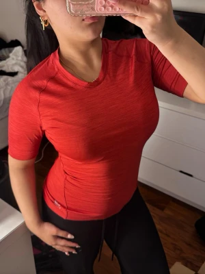 Röd sportig t-shirt med kort ärm - Snygg röd sport-tshirt med korta ärmar och rund hals. Tillverkad i ett stretchigt och snabbtorkande material som passar perfekt till träning eller gym. Figurnära passform som framhäver kroppen och ger en sportig look.