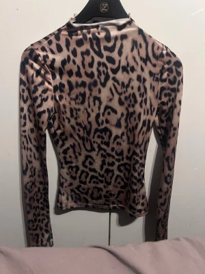 Leopardmönstrad långärmad topp H&M - Säljer en snygg långärmad topp från H&M med leopardmönster i beige och svart. Toppen har en tight passform och är tillverkad i ett mjukt, stretchigt syntetmaterial. Perfekt för dig som vill sticka ut med ett djurmönstrat plagg.