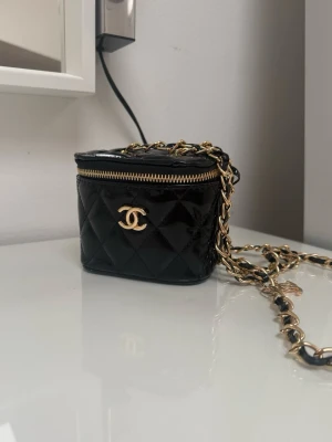 Svart quiltad vanity väska med kedja - Säljer en svart quiltad mini/vanity väska i glansigt konstläder. 