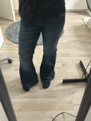 Mörkblå bootcut jeans - Säljer ett par mörkblå bootcut jeans med snygga slitningar och kontrastsömmar. Jeansen har klassisk femficksdesign och är low waist. Materialet är denim med lite stretch för extra komfort. Perfekta för dig som gillar en avslappnad men trendig look.