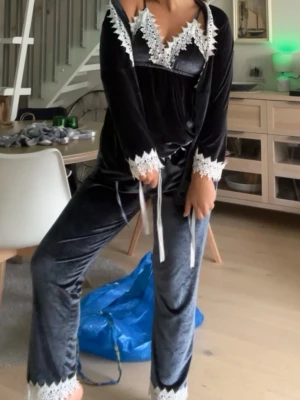 Mörkgrå sammets pyjamas med spets - Snyggt pyjamasset från Dennis Maglic i mörkgrå/ blåaktig sammet med vita spetsdetaljer. Setet består av byxor, linne och en matchande kimono med knytband. Spetsdetaljer på både linne, ärmar och ben för en extra lyxig känsla. Perfekt för mysiga kvällar hemma och nu till hösten! Inköpt för 899 men säljer för 499 alltså 400kr billigare!