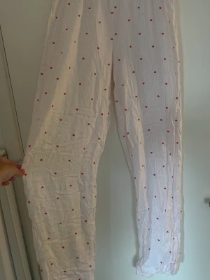Vita pyjamasbyxor med små röda hjärtan - Säljer ett par vita pyjamasbyxor med små röda hjärtan som mönster. Byxorna är från H&M i storlek XS/S.