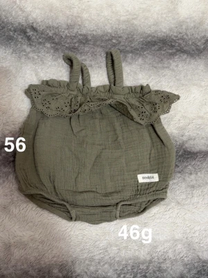 Olivgrön byxdress med volang - Supersöt olivgrön byxdress i muslin med broderad volang upptill och smala axelband. Perfekt för varma dagar och enkel att matcha med andra plagg. Liten etikett med texten 'newbie' framtill.🌸 Fint använt skick. Storlek 56