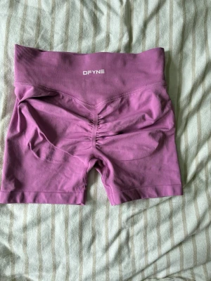 Lila träningstights från DFYNE - Säljer ett par lila träningstights från DFYNE med hög midja och scrunch-detalj bak. Shortsen är tillverkade i ett stretchigt material som passar perfekt för gym eller annan träning. Bekväm passform och ribbad linning för extra stöd.