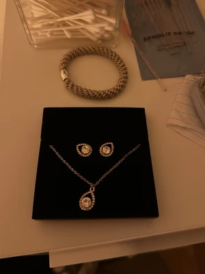 Silverfärgat smyckeset med stenar - Säljer ett elegant smyckeset med halsband och matchande örhängen i silverfärg. Både halsbandet och örhängena har gnistrande stenar i droppformad design med små kristaller runt om. Perfekt för dig som vill ha en stilren och glittrig look.