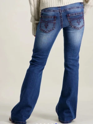 Blå bootcut jeans med röd söm - Snygga blå bootcut jeans med markerade röda sömmar och broderade bakfickor. Jeansen har en klassisk femficksmodell och lätt slitna detaljer för en cool look. Tillverkade i denim med stretch för skön passform. Ink frakt och priset kan diskuteras 