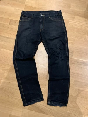 Mörkblå Cheap mondey jeans  - Säljer ett par mörkblå Cheap monday jeans med raka ben och rå, ofållad kant längst ner. Klassisk femficksmodell med kontrastsömmar och knappgylf. Perfekta för en avslappnad och trendig look.
