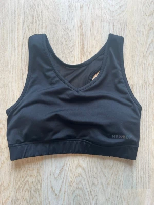 Svart sport-bh från Newbody - En svart sport-bh från Newbody med breda axelband och rundad halsringning. Bh:n har en elastisk resår under bysten och meshdetaljer i ryggen för extra ventilation. Tillverkad i ett stretchigt funktionsmaterial som passar perfekt till träning. Paddingen är även uttagbar. Tveka inte på att skriva en fråga eller be om fler bilder.🌸🌸