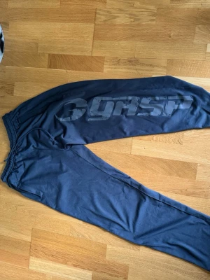 Svarta mjukisbyxor från GASP - Säljer ett par grå mjukisbyxor från GASP med stort tryck längs ena benet. Byxorna har resår i midjan och raka ben, perfekta för chill eller gym. Materialet är mjukt och skönt, och de har en avslappnad passform. Hör av er vid mer intresse 