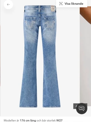 Blå utsvängda jeans True Religion lågmidjade  - Säljer ett par ljusblå utsvängda jeans från True Religion med snygga slitningar och dekorativa diamanter på bakfickorna. Klassisk femficksmodell med patch på linningen. Perfekta för dig som gillar en trendig och avslappnad look.