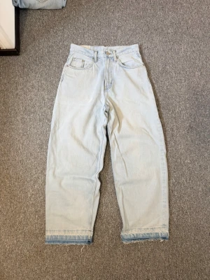 Baggy ljusblå jeans från H&M - Baggy loose fit jeans från H&M i ljusblå denim. Jeansen har hög midja, raka ben och avslappnad passform. Klassisk femficksmodell och rå kant nertill för en trendig look. Perfekta för dig som gillar en chill och oversized stil.