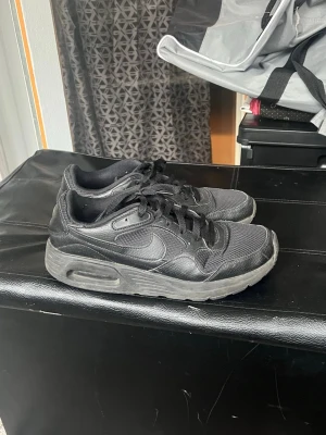 Svarta Nike Air Max sneakers - Säljer ett par svarta Nike Air Max sneakers med klassisk låg profil och tydlig Air Max-dämpning i sulan. Skorna har mesh och syntetmaterial på ovansidan, samt svarta skosnören och diskret Nike-logga på sidan. Perfekt för dig som gillar streetstyle.