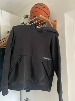 Svart hoodie Sail Racing Hoodie 160 CM - Säljer en svart sailracing hoodie med stor huva och dragsko. Hoodien har en stor magficka och en liten logga på bröstet. Tillverkad i mjukt material som passar perfekt för chill dagar eller träning.