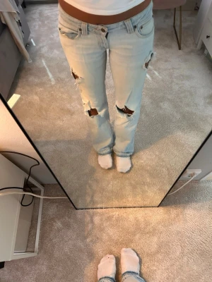 Ljusblå slitna bootcut jeans - Säljer ett par ljusblå bootcut jeans med slitningar och hål på framsidan. Jeansen har låg midja och jättesnygga detaljer på fickorna. Jag är 173cm lång ungefär och har normalt storlek 36 i tex Zara jeans❤️