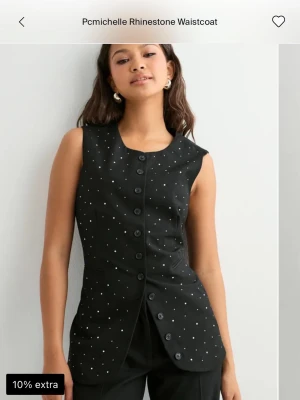 Svart väst med paljetter och knappar - Snygg svart väst med glittriga paljettdetaljer och knäppning framtill. Västen har en figurnära passform och är ärmlös, perfekt för att lyfta vilken outfit som helst. Stilsäker och trendig design som sticker ut.