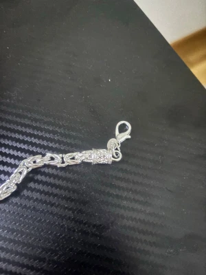 Äkta Silver kedjehalsband - Säljer ett stilrent halsband i silver med en robust kedjedesign. Halsbandet har ett dekorativt mönster på länkarna och ett smidigt karbinlås. Perfekt för dig som gillar en clean och modern look.