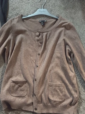Brun kofta från H&M Basic - Mysig brun kofta från H&M Basic med rund halsringning och knappar framtill. Koftan har två praktiska fickor framtill och är tillverkad i ett mjukt, tunt material. Perfekt att slänga över en t-shirt eller linne.