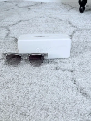 Transparenta CHIMI solglasögon - Snygga solglasögon från CHIMI med transparent båge och mörktonade glas. Rektangulär form som ger en modern vibe. Kommer med originaletui och putsduk. Perfekta för dig som vill ha en clean och stilren look.