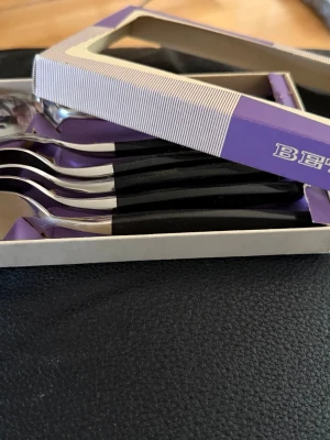 Bestickset i svart och silverfärgade  - Säljer två nya   set med sex  bestick i varje originalförpackning, sex gafflar och sex knivar, dom är ifrån märket Betina. Besticken har svarta handtag och blanka silverfärgade delar i metall. Perfekt till köket eller som extra uppsättning till picknick eller utflykt.