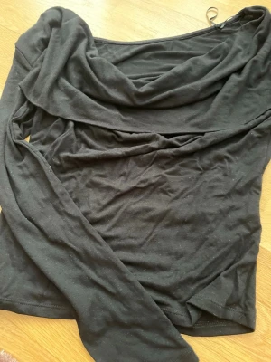 Svart långärmad topp Gina Tricot - Svart långärmad topp från Gina Tricot med snygg draperad halsringning. Tillverkad i mjukt material som sitter skönt på kroppen. Perfekt för dig som gillar stilrena och trendiga plagg med en twist.