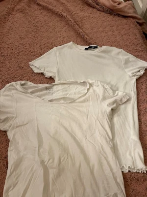 Två vita kortärmade t-shirts - Säljer två vita t-shirts i olika modeller. Ena är ribbad med vågiga kanter på ärmar och nederkant, den andra är basic med rund hals. Perfekta till jeans eller kjol och passar till alla tillfällen.