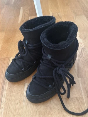 Svarta moon boots med snörning - Säljer ett par svarta moon boots med högt skaft och tjocka snören. Insidan är fodrad med mjukt material för extra värme och komfort. Utsidan är i mockaliknande material och sulan är i gummi. Perfekta för kalla dagar när du vill hålla stilen.